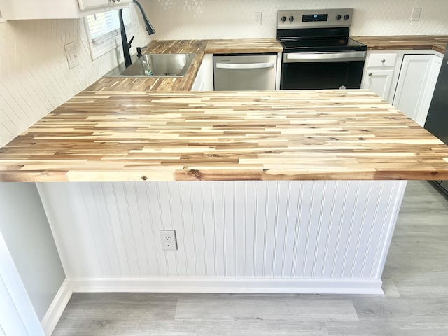 kitchen featuring wood counters, stainless steel appliances, sink, light hardwood / wood-style flooring, and white cabinetry