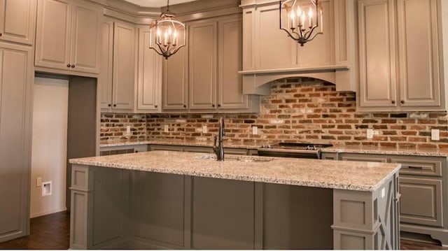 kitchen featuring light stone counters, a kitchen island with sink, sink, decorative light fixtures, and range