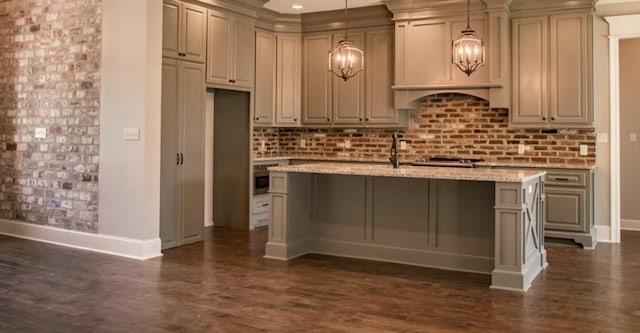 kitchen featuring light stone countertops, hanging light fixtures, dark hardwood / wood-style floors, an island with sink, and decorative backsplash