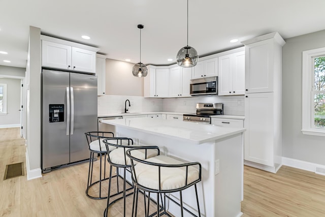 kitchen featuring white cabinets, decorative light fixtures, and stainless steel appliances