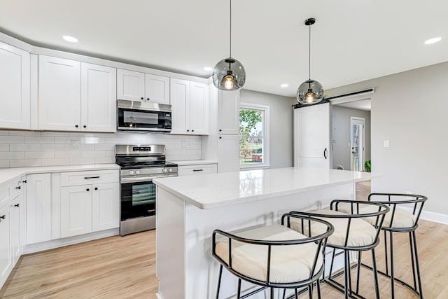 kitchen featuring a center island, hanging light fixtures, stainless steel appliances, a breakfast bar area, and white cabinets