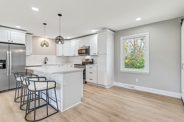 kitchen with white cabinets, appliances with stainless steel finishes, decorative light fixtures, and light hardwood / wood-style floors