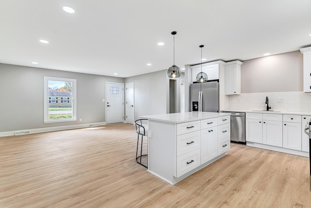 kitchen with white cabinetry, sink, pendant lighting, a kitchen island, and appliances with stainless steel finishes