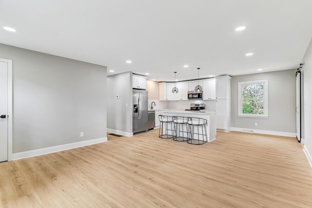 kitchen with appliances with stainless steel finishes, pendant lighting, light hardwood / wood-style floors, a kitchen island, and a breakfast bar area