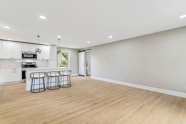 kitchen with appliances with stainless steel finishes, a barn door, decorative light fixtures, white cabinets, and a breakfast bar area