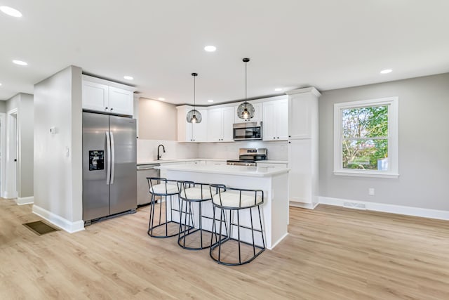 kitchen with hanging light fixtures, light hardwood / wood-style flooring, backsplash, white cabinets, and appliances with stainless steel finishes