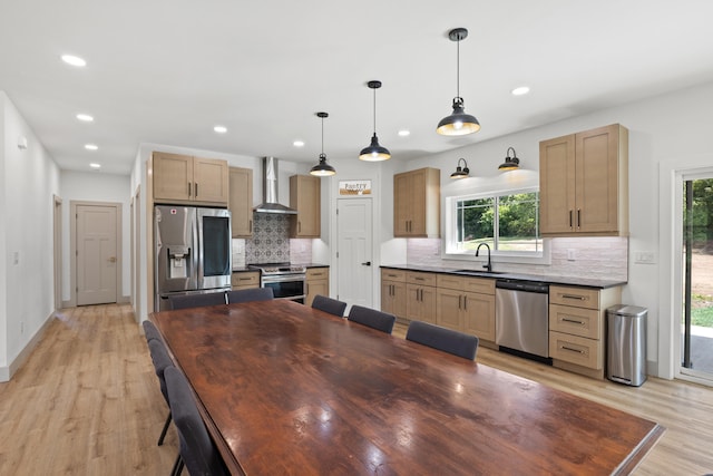 kitchen with sink, wall chimney exhaust hood, a wealth of natural light, appliances with stainless steel finishes, and decorative light fixtures