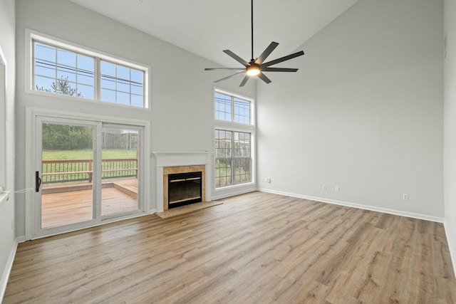 unfurnished living room with ceiling fan, light wood-type flooring, a premium fireplace, and high vaulted ceiling