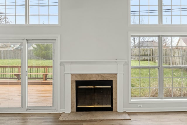 unfurnished living room featuring a high end fireplace, a healthy amount of sunlight, and hardwood / wood-style flooring