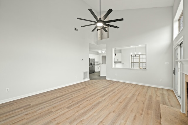 unfurnished living room featuring ceiling fan with notable chandelier, light hardwood / wood-style floors, and high vaulted ceiling