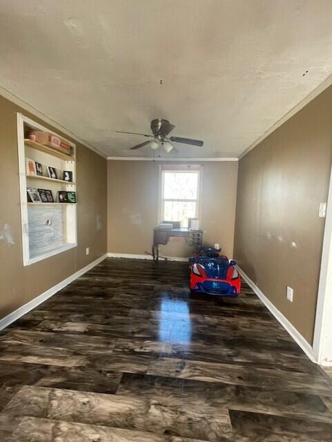 empty room featuring built in shelves, dark hardwood / wood-style flooring, ceiling fan, and ornamental molding