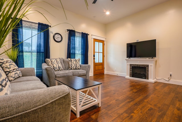 living room with dark hardwood / wood-style flooring, a stone fireplace, and ceiling fan