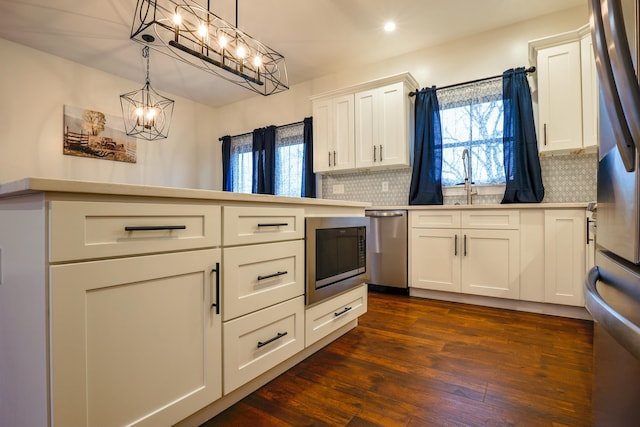 kitchen with dark hardwood / wood-style flooring, backsplash, stainless steel appliances, white cabinetry, and hanging light fixtures