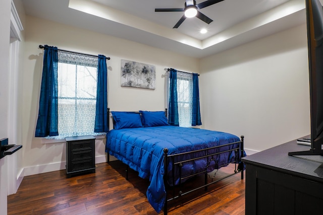 bedroom with ceiling fan, a raised ceiling, and dark wood-type flooring