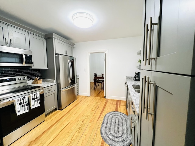 kitchen featuring gray cabinetry, light stone countertops, tasteful backsplash, light hardwood / wood-style flooring, and appliances with stainless steel finishes