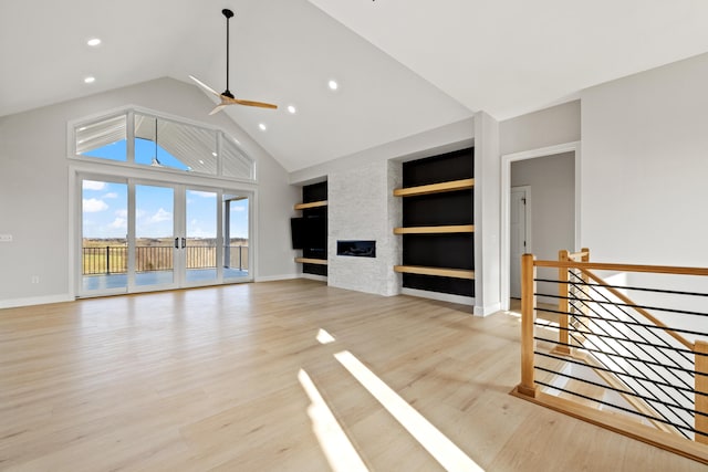 unfurnished living room with light wood-type flooring, built in shelves, a large fireplace, ceiling fan, and a high ceiling