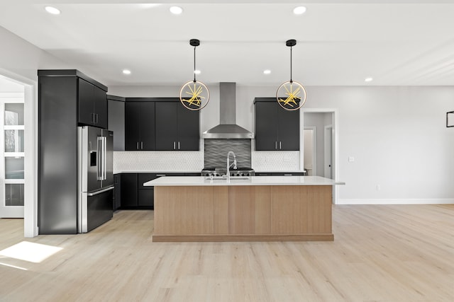 kitchen with a kitchen island with sink, hanging light fixtures, light hardwood / wood-style flooring, wall chimney exhaust hood, and high end fridge