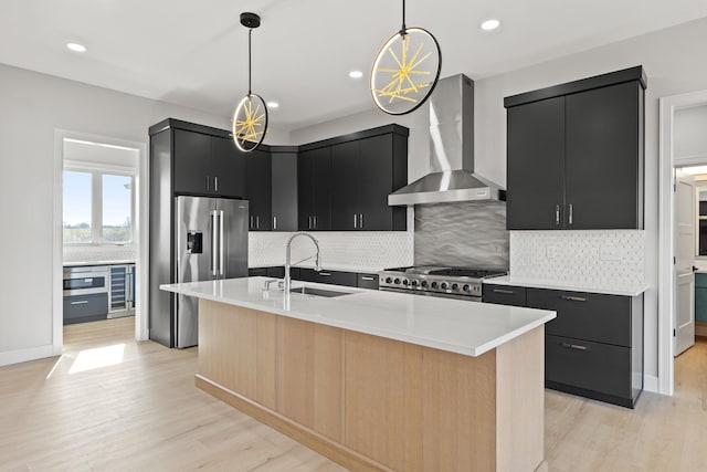 kitchen with sink, hanging light fixtures, wall chimney range hood, and a center island with sink