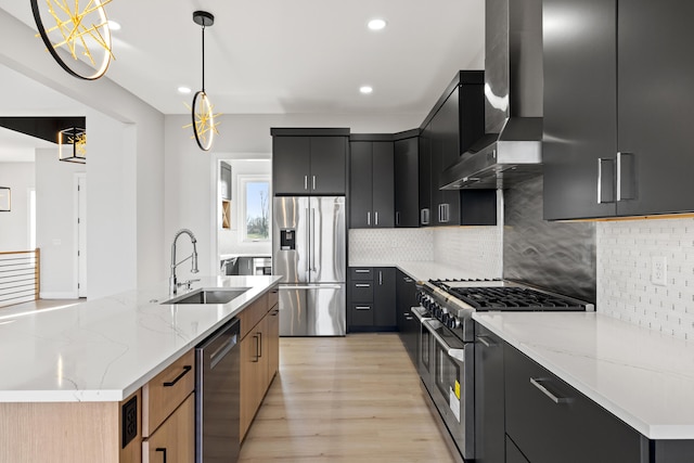 kitchen featuring a center island with sink, wall chimney exhaust hood, appliances with stainless steel finishes, decorative light fixtures, and light stone counters