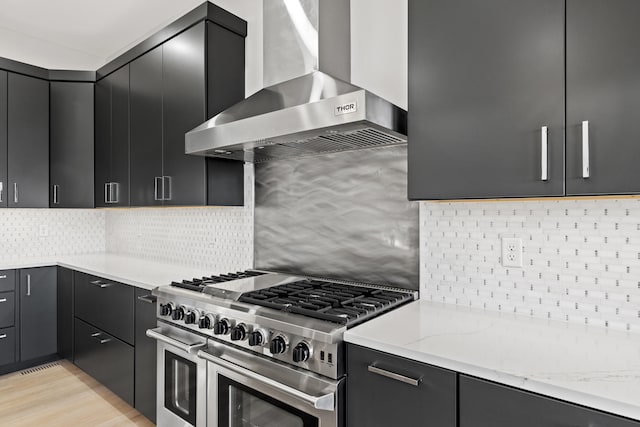 kitchen featuring high end range, backsplash, light stone counters, and wall chimney exhaust hood