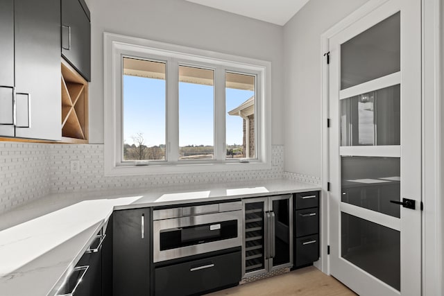 kitchen with decorative backsplash, light hardwood / wood-style flooring, wine cooler, and light stone counters