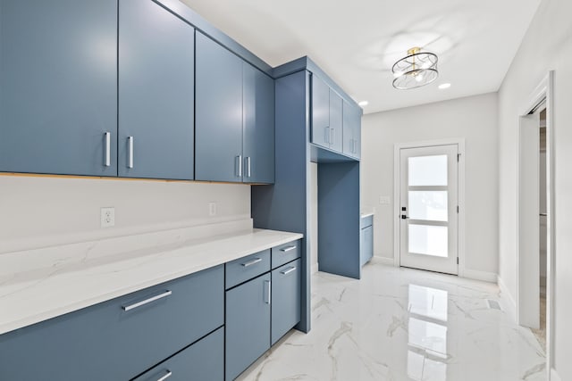 kitchen featuring light stone counters, blue cabinetry, and an inviting chandelier