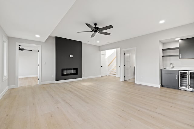 unfurnished living room featuring a large fireplace, light hardwood / wood-style floors, wine cooler, and ceiling fan