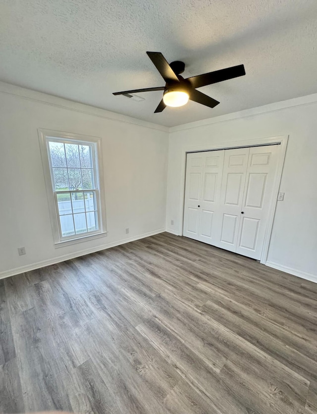 unfurnished bedroom featuring ornamental molding, a textured ceiling, ceiling fan, light hardwood / wood-style flooring, and a closet