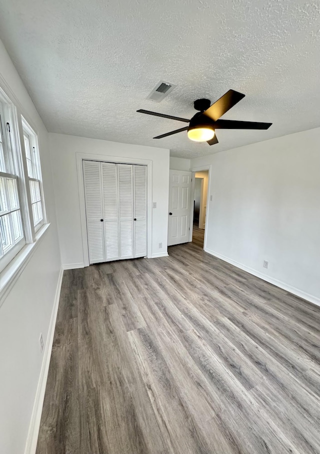 unfurnished bedroom with ceiling fan, light hardwood / wood-style floors, a textured ceiling, and a closet