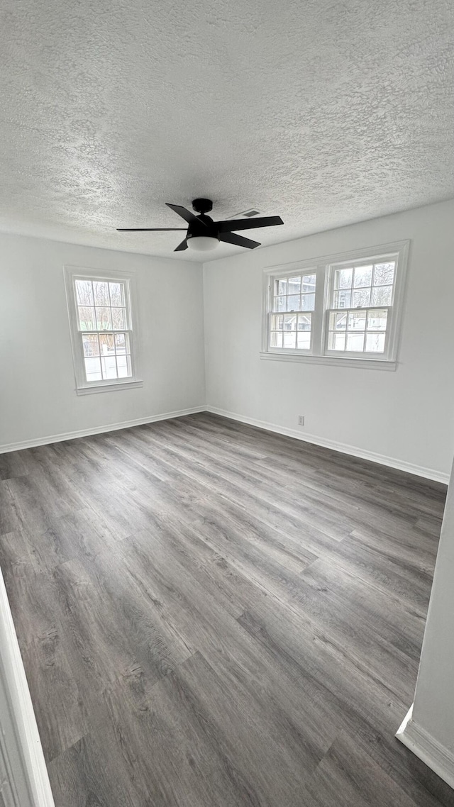 empty room with dark hardwood / wood-style flooring, ceiling fan, plenty of natural light, and a textured ceiling