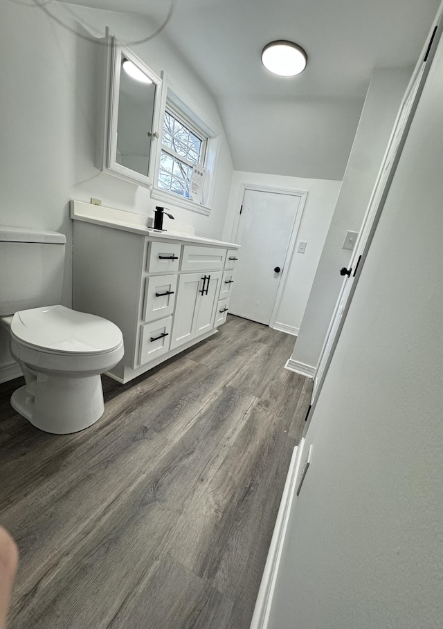 bathroom with hardwood / wood-style floors, vanity, vaulted ceiling, and toilet