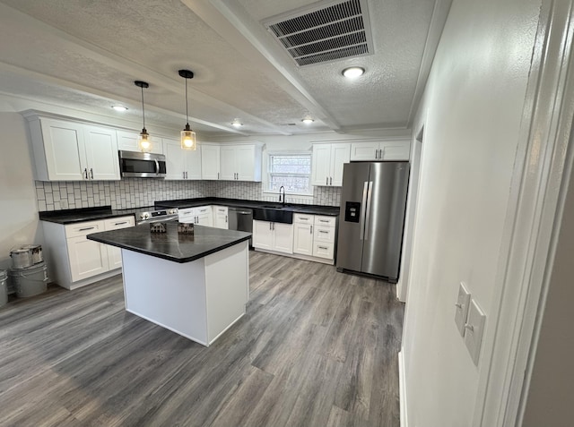 kitchen with pendant lighting, white cabinets, hardwood / wood-style flooring, appliances with stainless steel finishes, and a kitchen island