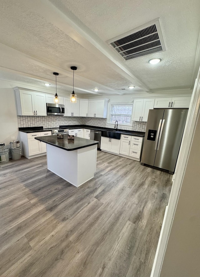 kitchen with sink, hanging light fixtures, white cabinets, a kitchen island, and appliances with stainless steel finishes