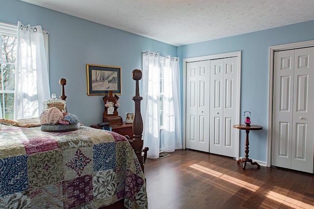 bedroom featuring multiple closets, dark hardwood / wood-style flooring, multiple windows, and a textured ceiling