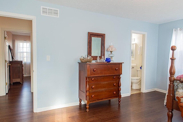 bedroom featuring connected bathroom, dark hardwood / wood-style flooring, and a textured ceiling