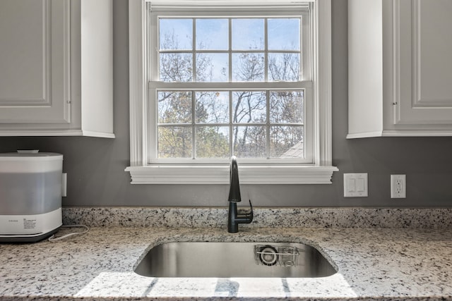 interior details featuring white cabinetry, light stone countertops, and sink