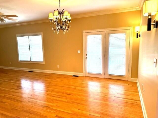unfurnished room featuring a wealth of natural light, hardwood / wood-style flooring, ceiling fan with notable chandelier, and ornamental molding