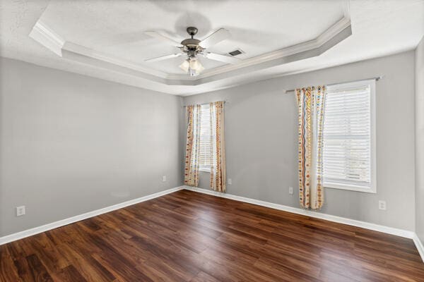 unfurnished room featuring a raised ceiling, ceiling fan, crown molding, and dark hardwood / wood-style floors