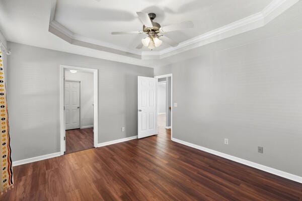 unfurnished bedroom with ornamental molding, a tray ceiling, ceiling fan, and dark wood-type flooring