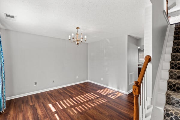 empty room featuring a textured ceiling, an inviting chandelier, and dark wood-type flooring