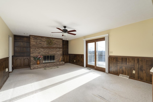 unfurnished living room with light carpet, a brick fireplace, ceiling fan, wooden walls, and built in features