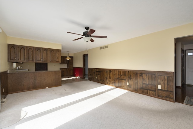 unfurnished living room with wood walls, sink, ceiling fan, and light carpet