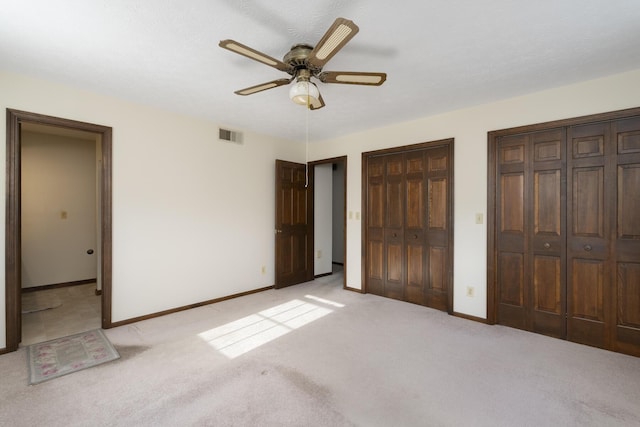 unfurnished bedroom with light carpet, two closets, and ceiling fan