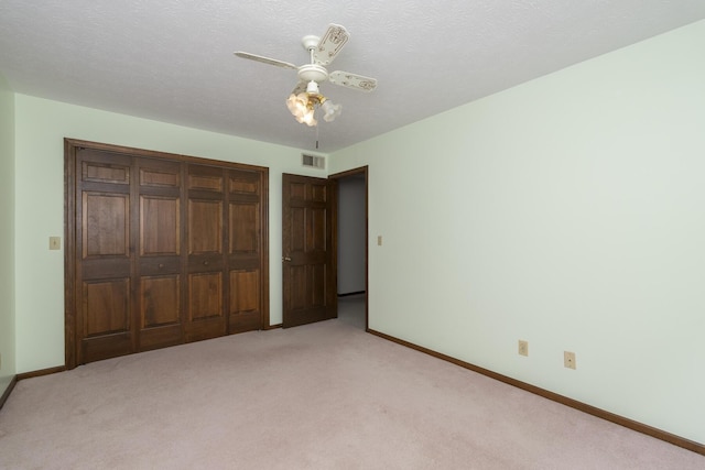 unfurnished bedroom featuring light carpet, a textured ceiling, a closet, and ceiling fan