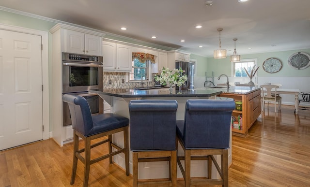 kitchen with appliances with stainless steel finishes, crown molding, a center island with sink, white cabinets, and hanging light fixtures