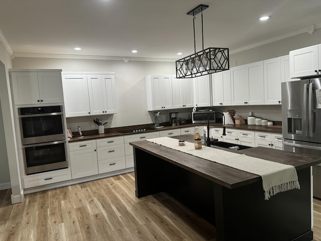 kitchen with sink, stainless steel appliances, butcher block countertops, decorative light fixtures, and a center island with sink