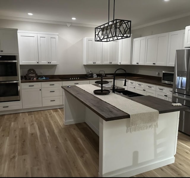 kitchen with a center island with sink, sink, appliances with stainless steel finishes, decorative light fixtures, and white cabinetry