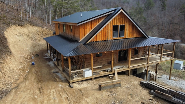 back of house with board and batten siding, metal roof, and a view of trees