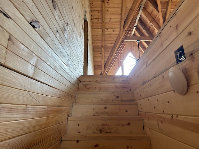 stairs with beam ceiling, wooden ceiling, and wood walls