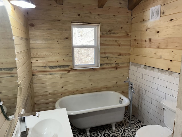 bathroom with wood walls, a soaking tub, a sink, and toilet